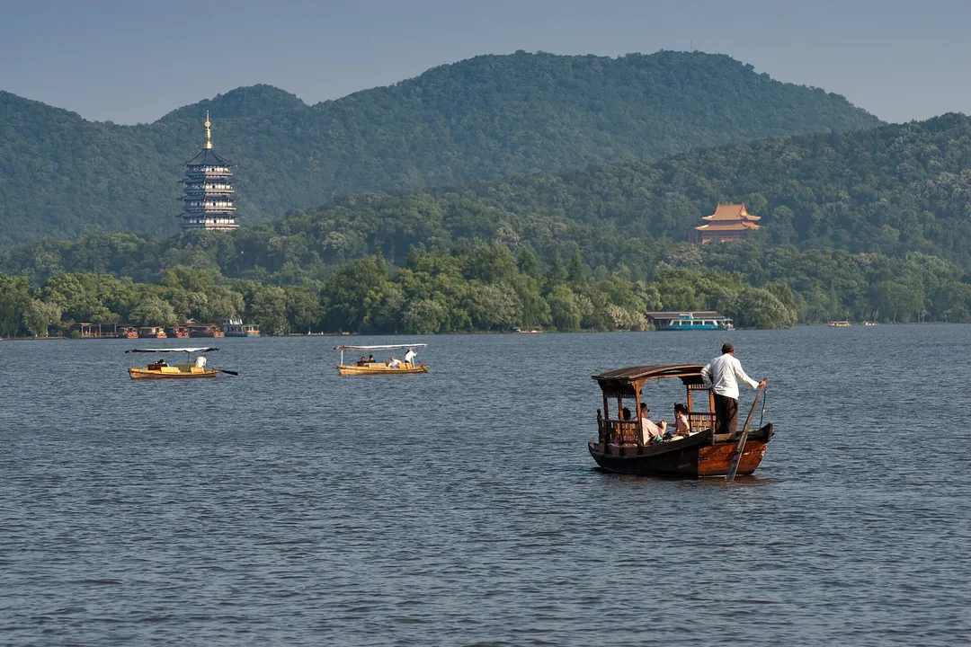 A wooden canopy boat with a boatman sculling on West Lake, Leifeng Pagoda across the water