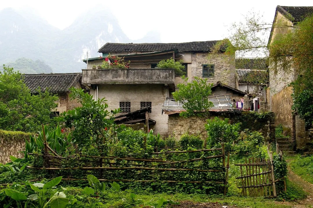 Old village houses behind a fenced garden with karst peaks in haze above