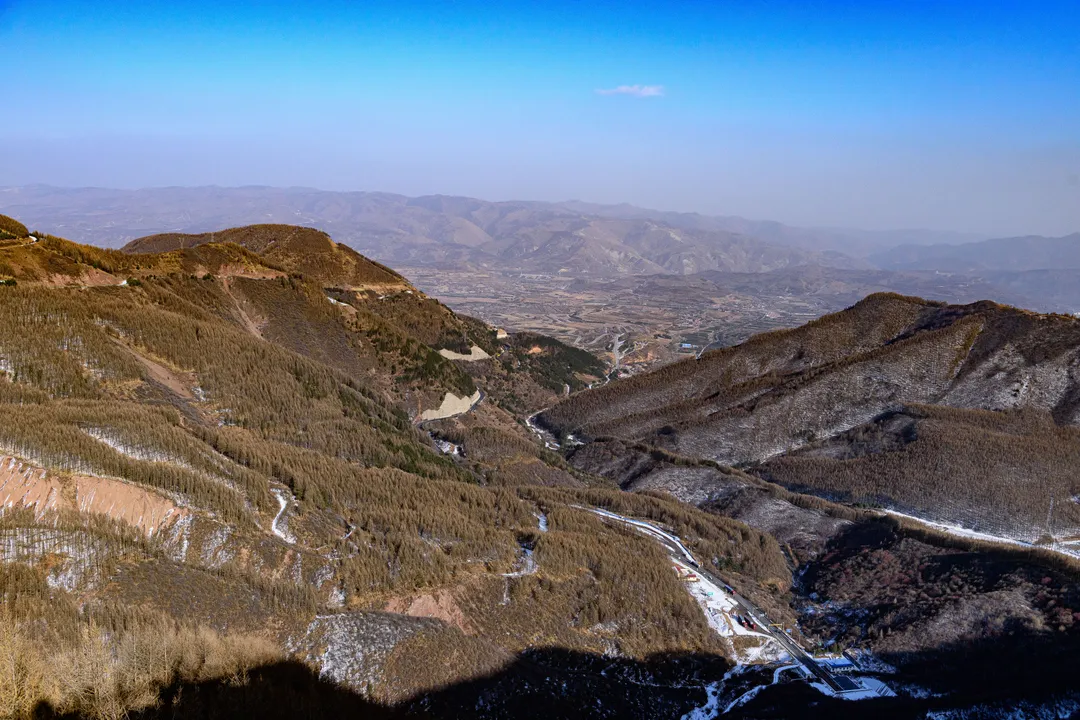 Ridges of the Liupan range with conifer forest and light snow, the valley plain far below, seen from an observation deck