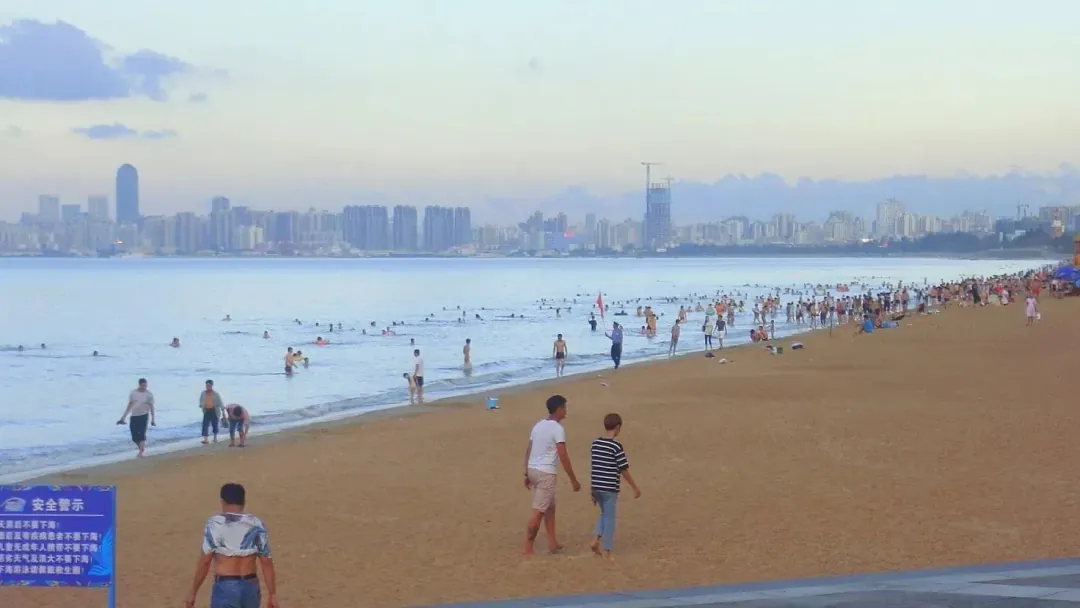 Swimmers on a wide sandy beach with the city skyline across the bay