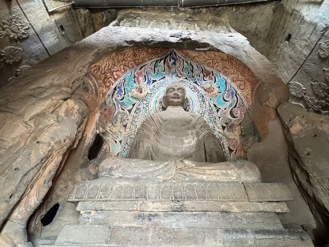 Un buda sedente desgastado en una hornacina de Xiangtangshan, con el halo pintado de llamas azules y rojas y acompañantes de piedra al lado