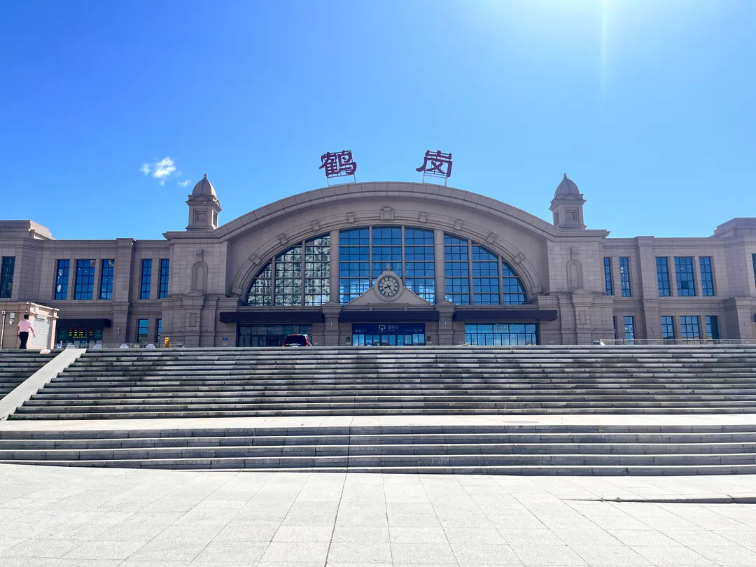 The stone facade of Hegang railway station with large red characters reading Hegang above the arched window and broad entrance steps