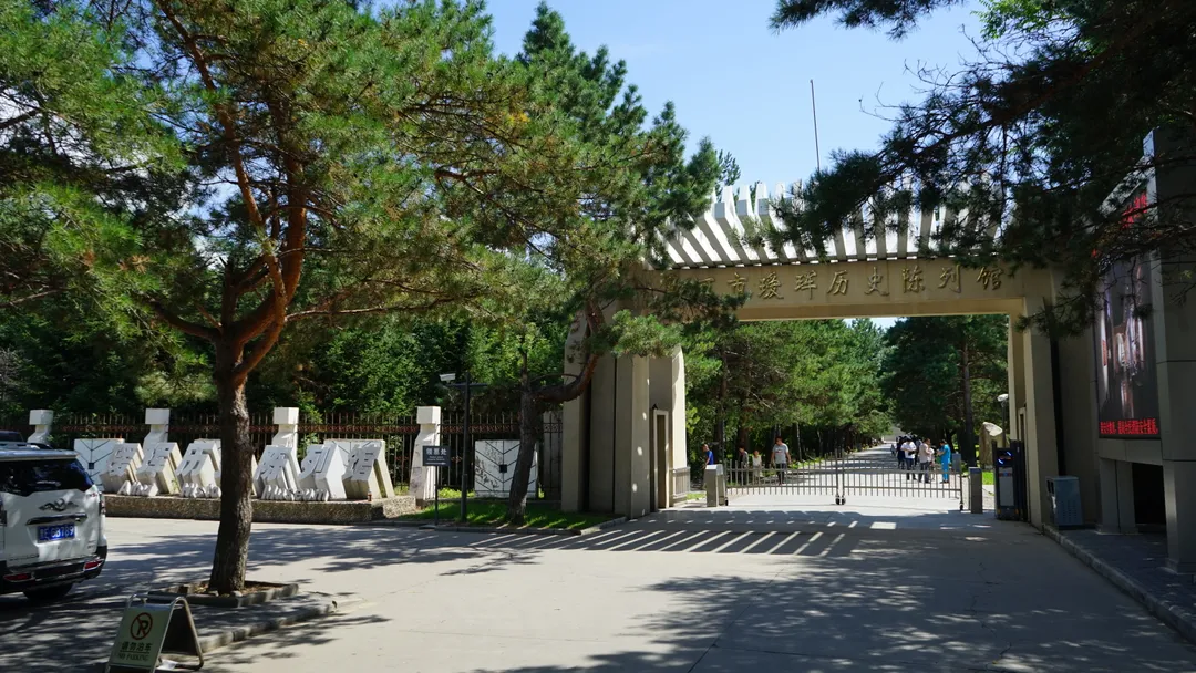 La puerta de entrada del Museo de Historia de Aihui con su inscripción tallada, entre pinos, con visitantes en el acceso