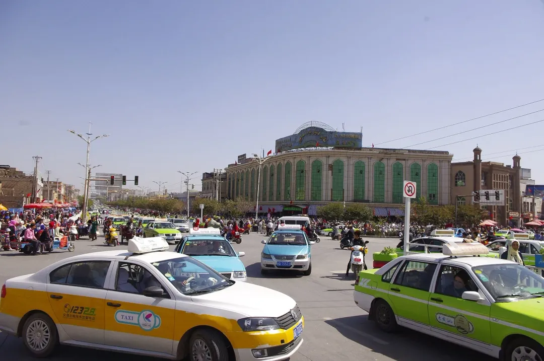 A taxi-filled square before the green arcade of the grand bazaar district in Kashgar