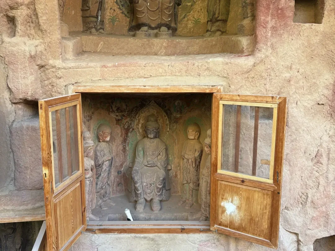 A carved Buddha niche with attendants behind wooden doors in the sandstone at Bingling Temple