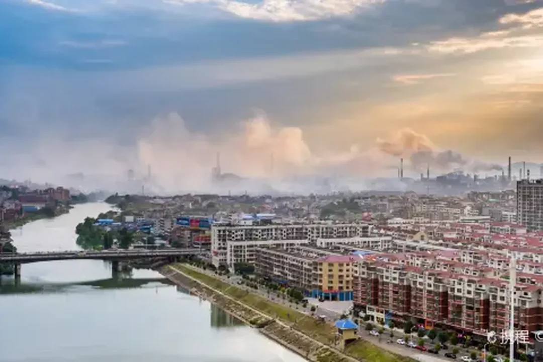The Lian riverfront of Loudi: apartment blocks along the embankment, a bridge over the river, the steel district's chimneys and steam on the horizon