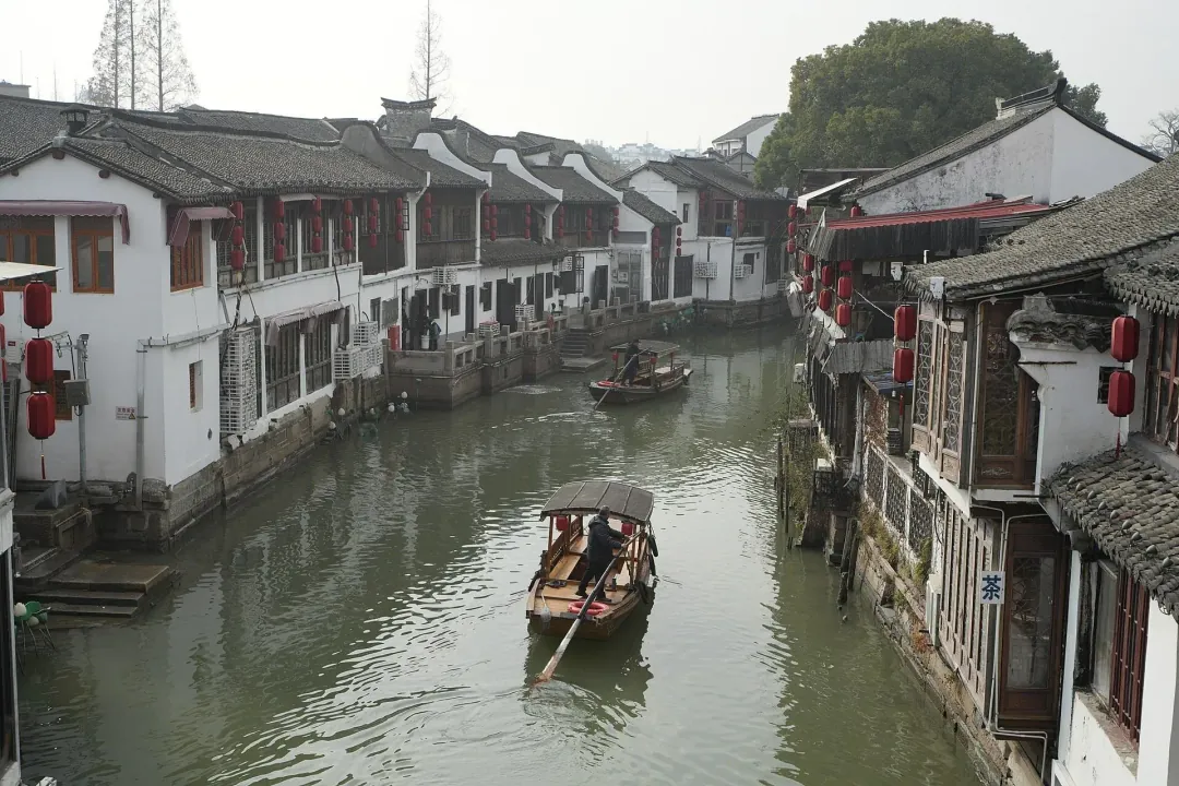 A wooden boat poled along the canal at Zhujiajiao, whitewashed houses and red lanterns on both banks
