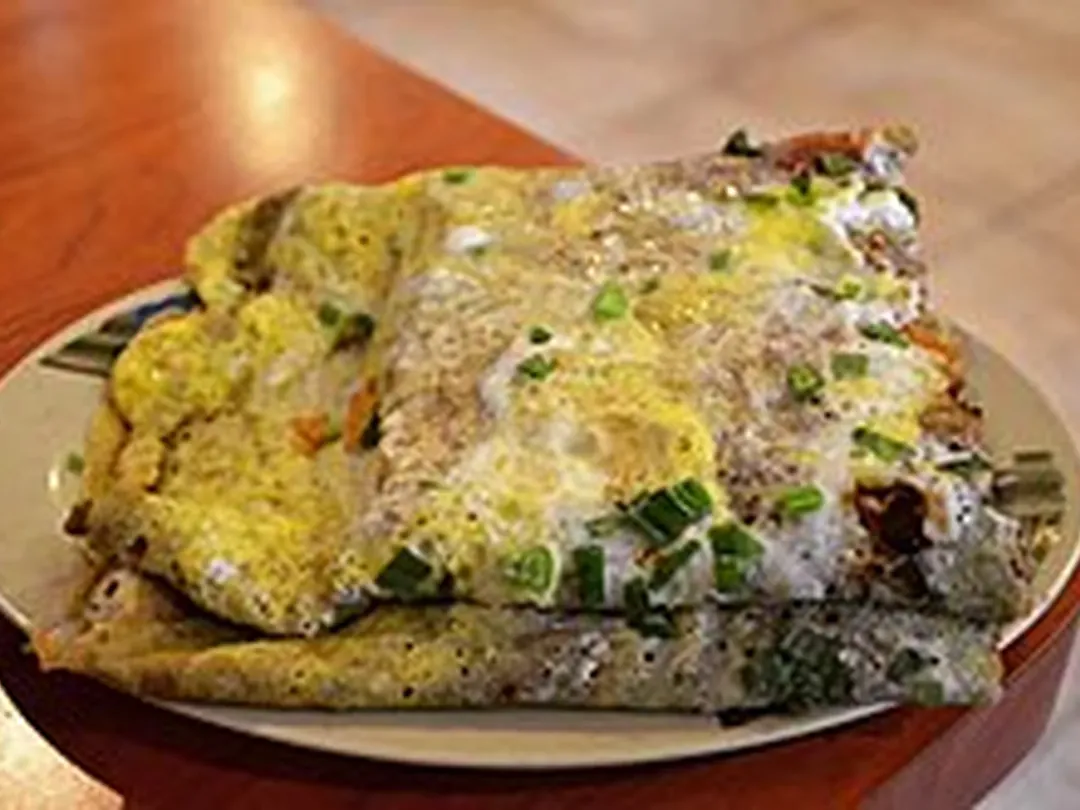 A folded jianbing guozi with cooked egg and chopped scallions on a plate, a Tianjin breakfast